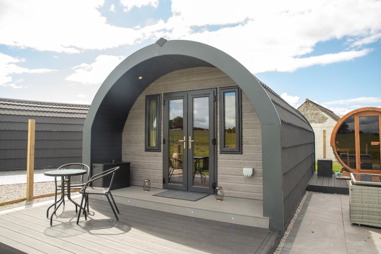 A glamping pod on a bright day, with the barrel sauna behind it