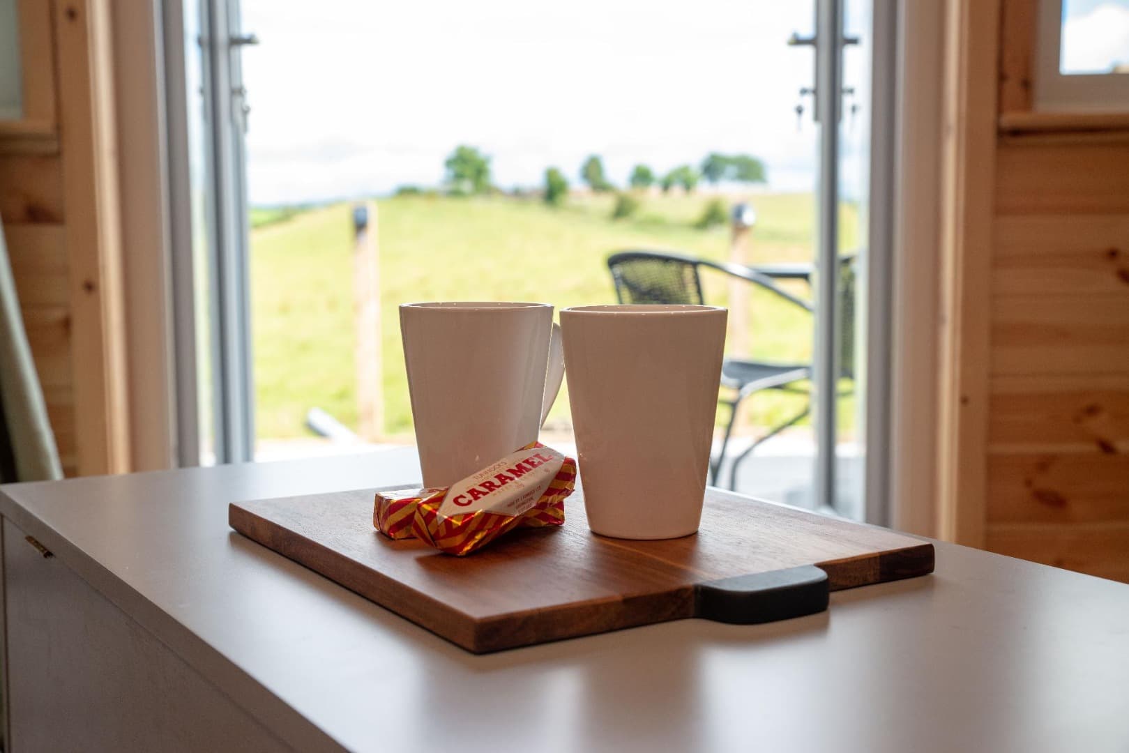 Mugs on the kitchen counter, with the countryside view through the doors
