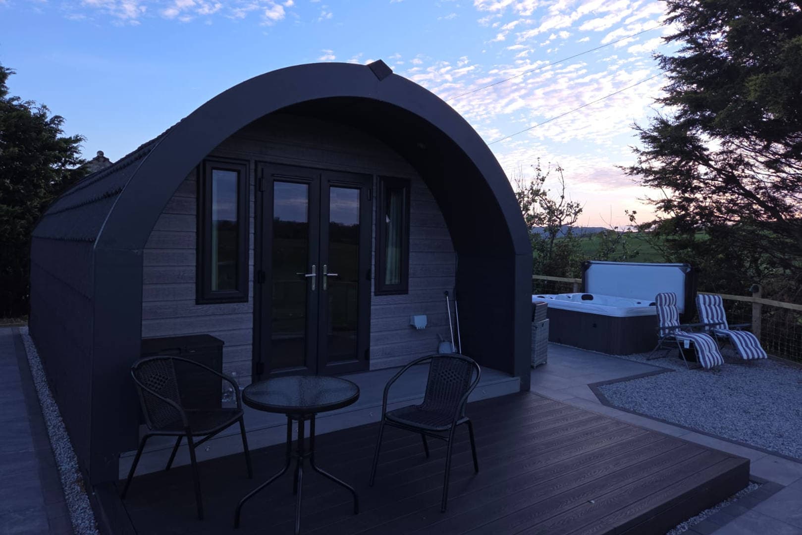A pod at dusk with the hot tub and loungers out on the deck