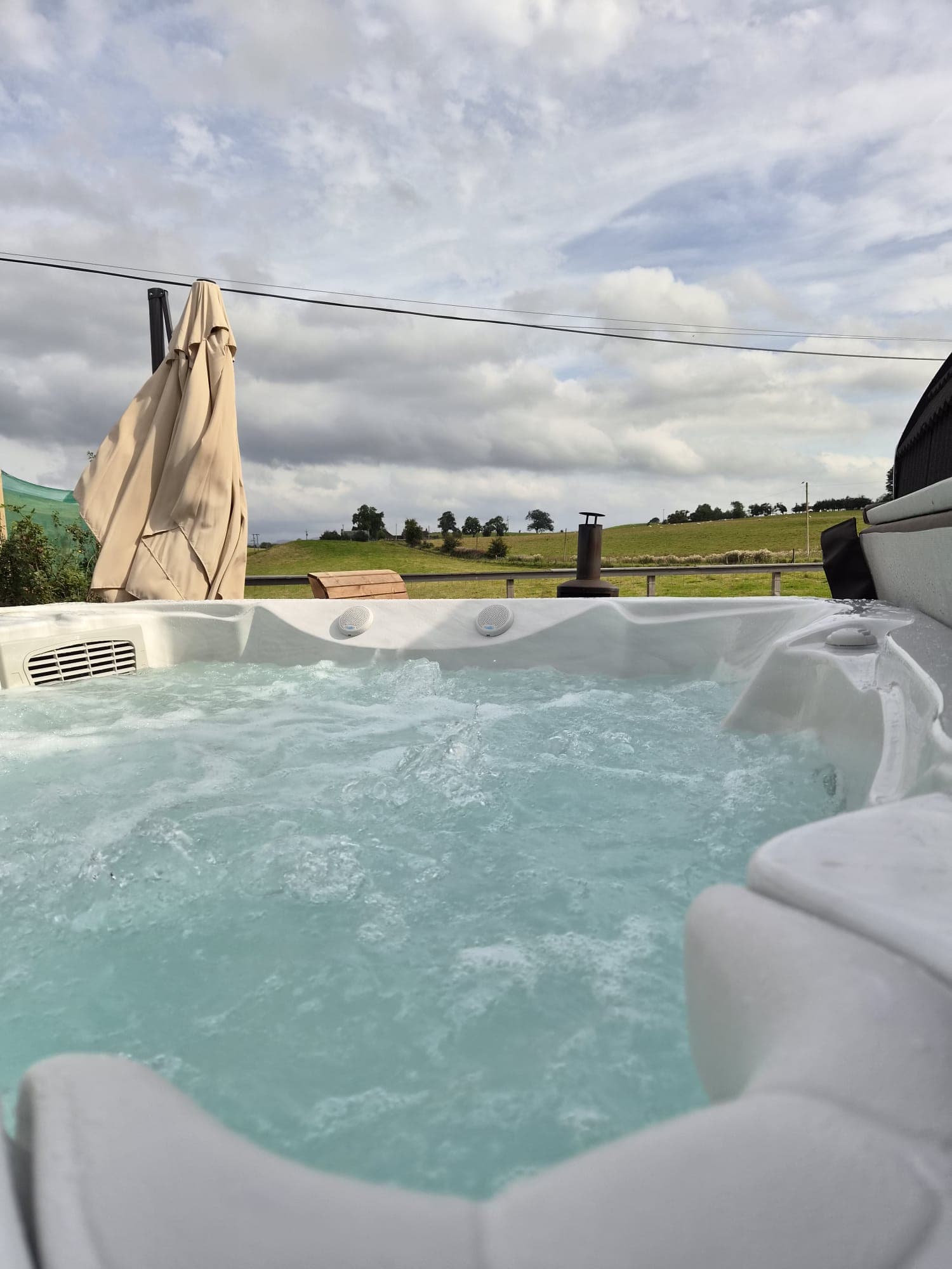 The Thistle Pod hot tub bubbling under an open sky, farmland behind